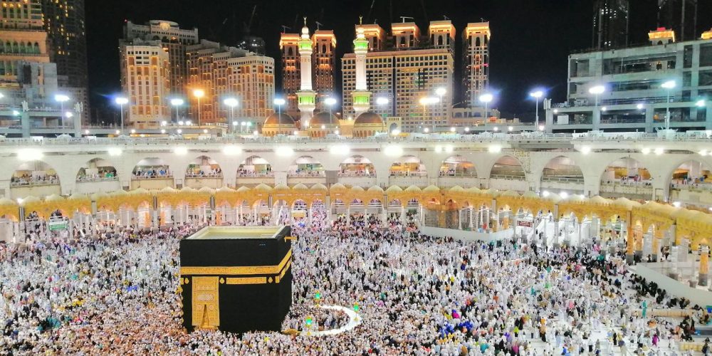 Aerial view of the Kaaba surrounded by pilgrims in Makkah at night, showcasing a religious gathering.